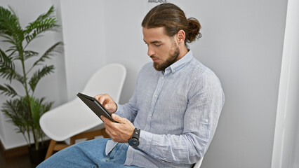 Young hispanic man using touchpad sitting on chair at waiting room