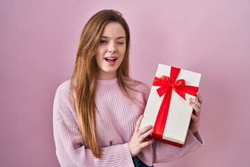 Young caucasian woman holding gift winking looking at the camera with sexy expression, cheerful and happy face.