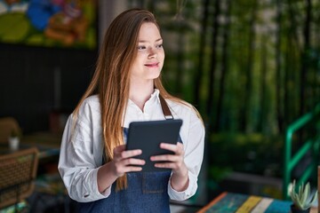 Young caucasian woman waitress smiling confident using touchpad at restaurant