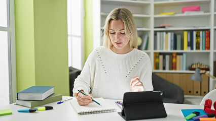 Young blonde woman student drawing on notebook using touchpad at library university