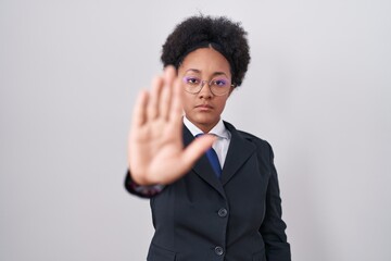 Beautiful african woman with curly hair wearing business jacket and glasses doing stop sing with palm of the hand. warning expression with negative and serious gesture on the face.