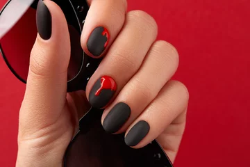 Foto op Canvas Close up womans hand with halloween manicure on red background holding sunglasses. Manicure, pedicure beauty salon concept © Darya Lavinskaya
