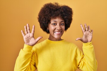 Young african american woman standing over yellow background showing and pointing up with fingers number ten while smiling confident and happy.