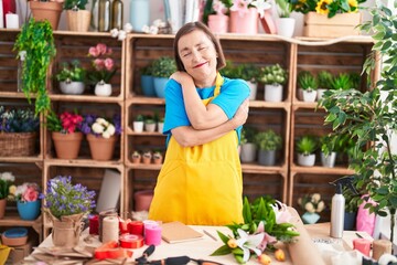 Middle age hispanic woman working at florist shop hugging oneself happy and positive, smiling confident. self love and self care