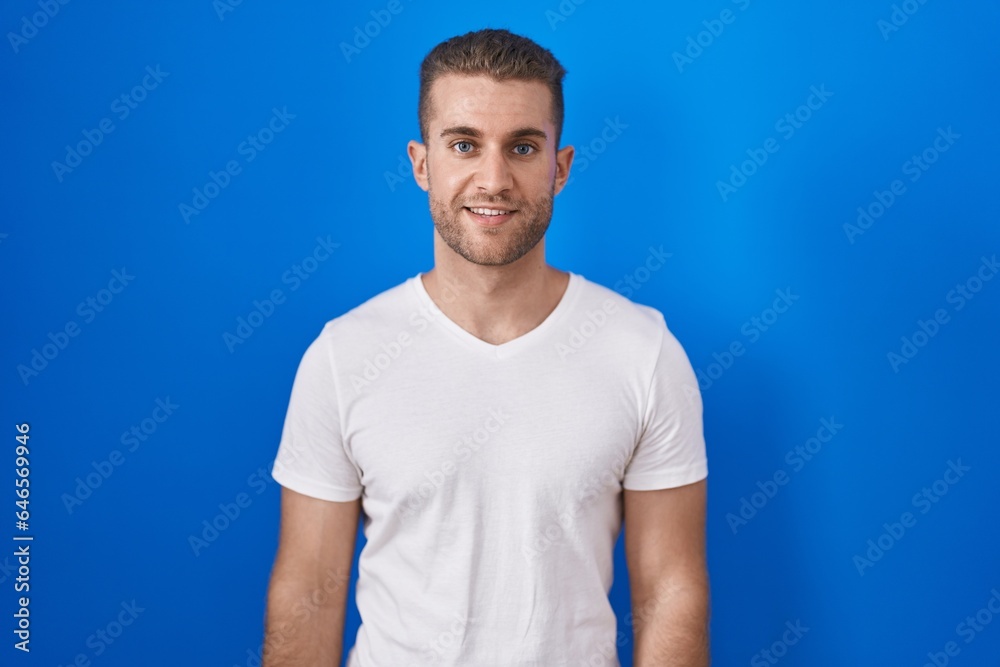 Wall mural Young caucasian man standing over blue background with a happy and cool smile on face. lucky person.