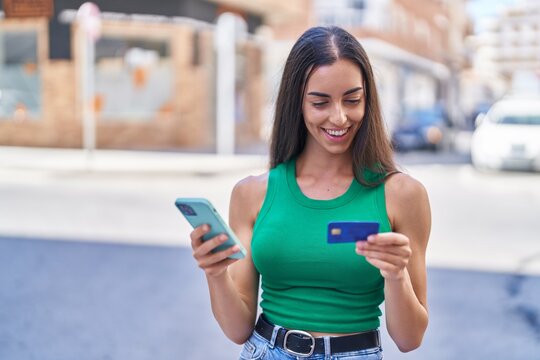 Young beautiful hispanic woman using smartphone and credit card at street