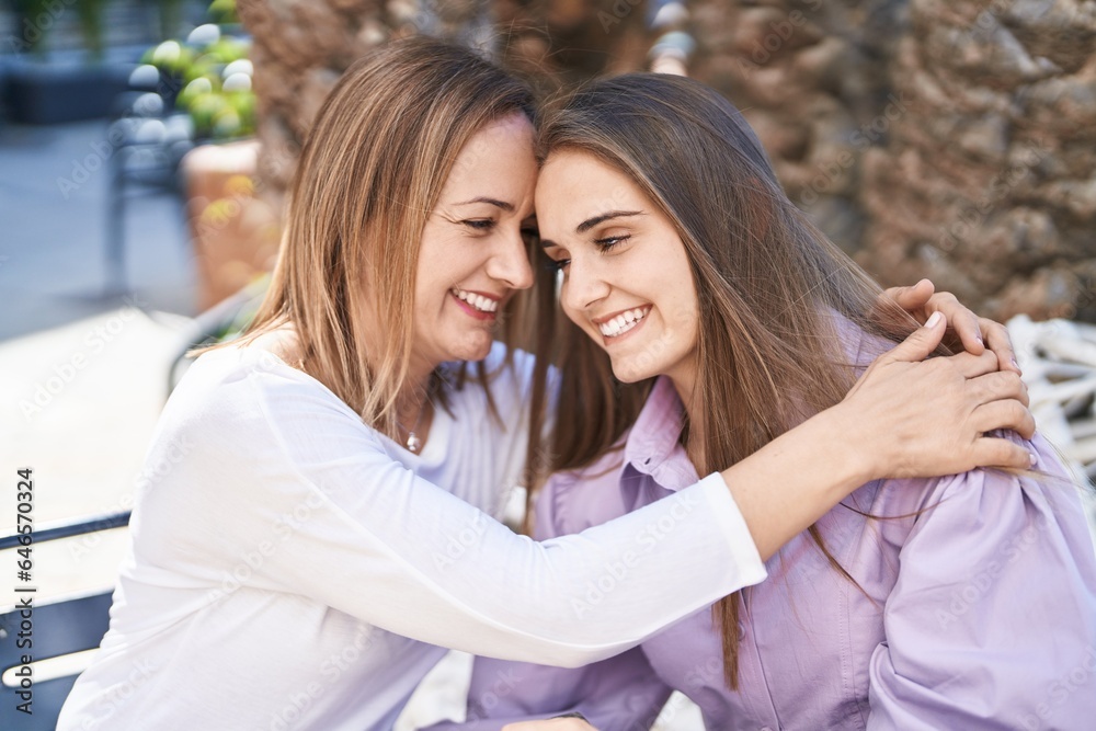 Wall mural two women mother and daughter hugging each other sitting on table at coffee shop terrace