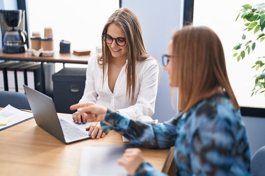 Two women business workers using laptop speaking at office