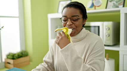 African american woman smiling confident eating banana at dinning room