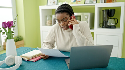 Fototapeta premium African american woman talking on smartphone reading document at dinning room