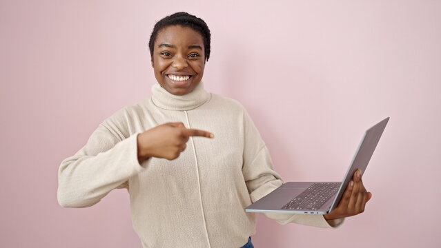 African american woman smiling pointing to laptop over isolated pink background