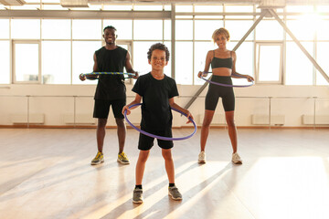 sporty african american family in sports uniform twists hula hoop and does exercises in the gym