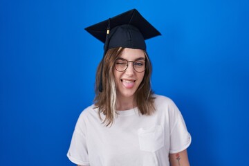 Blonde caucasian woman wearing graduation cap sticking tongue out happy with funny expression. emotion concept.