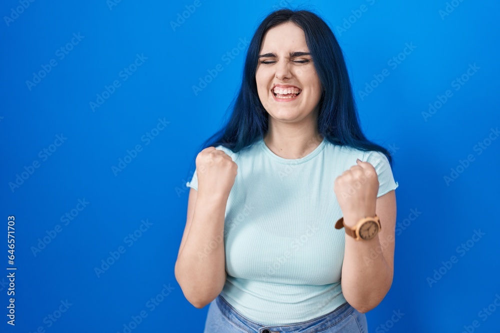 Sticker young modern girl with blue hair standing over blue background very happy and excited doing winner g