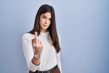 Young brunette woman standing over blue background showing middle finger, impolite and rude fuck off expression