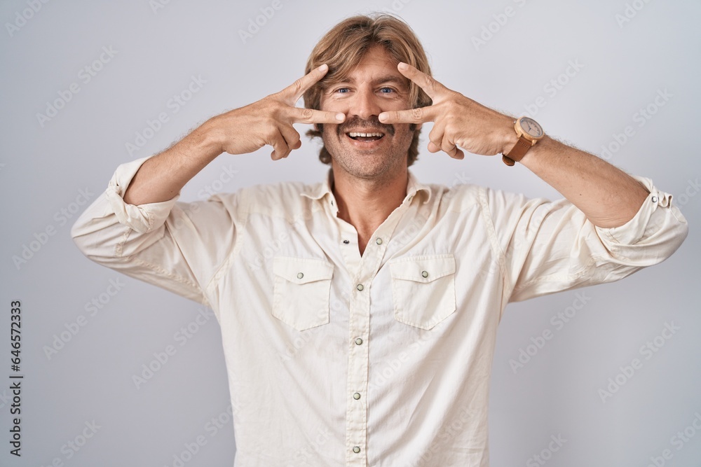 Sticker middle age man standing over isolated background doing peace symbol with fingers over face, smiling 