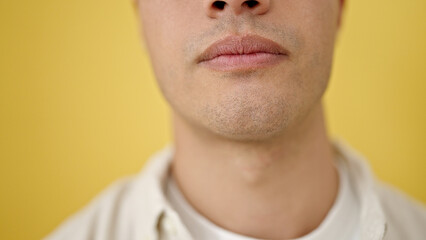 Obraz premium Young hispanic man close up of serious expression over isolated yellow background