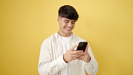 Young hispanic man using smartphone smiling over isolated yellow background