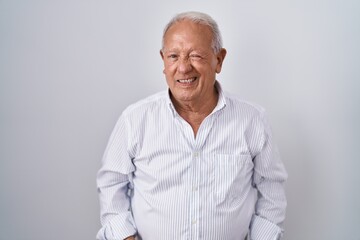 Senior man with grey hair standing over isolated background winking looking at the camera with sexy expression, cheerful and happy face.