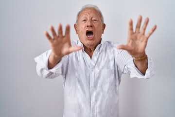 Fototapeta premium Senior man with grey hair standing over isolated background doing stop gesture with hands palms, angry and frustration expression