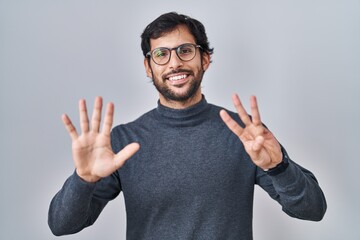 Naklejka premium Handsome latin man standing over isolated background showing and pointing up with fingers number eight while smiling confident and happy.