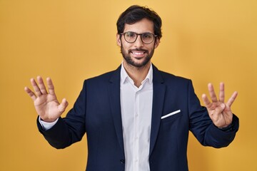 Handsome latin man standing over yellow background showing and pointing up with fingers number nine while smiling confident and happy.