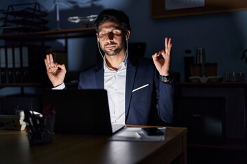 Handsome latin man working at the office at night relax and smiling with eyes closed doing meditation gesture with fingers. yoga concept.