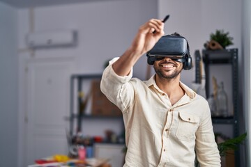 Young hispanic man artist using virtual reality glasses drawing at art studio