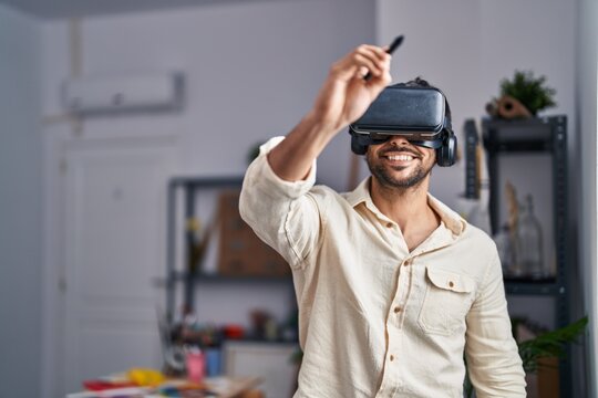 Young hispanic man artist using virtual reality glasses drawing at art studio