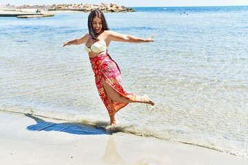 Young beautiful hispanic woman tourist wearing bikini dancing at seaside