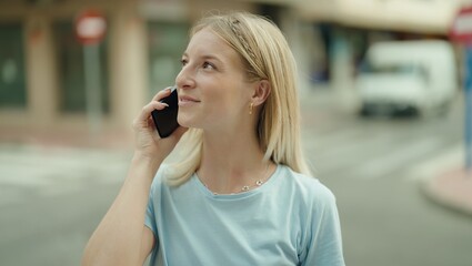 Young blonde woman smiling confident talking on the smartphone at street