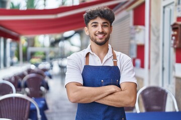 Young arab man waiter standing with arms crossed gesture at restaurant