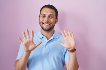 Hispanic man standing over pink background showing and pointing up with fingers number ten while smiling confident and happy.