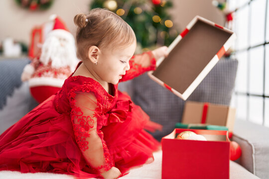 Adorable hispanic girl unpacking gift sitting on sofa by christmas tree at home
