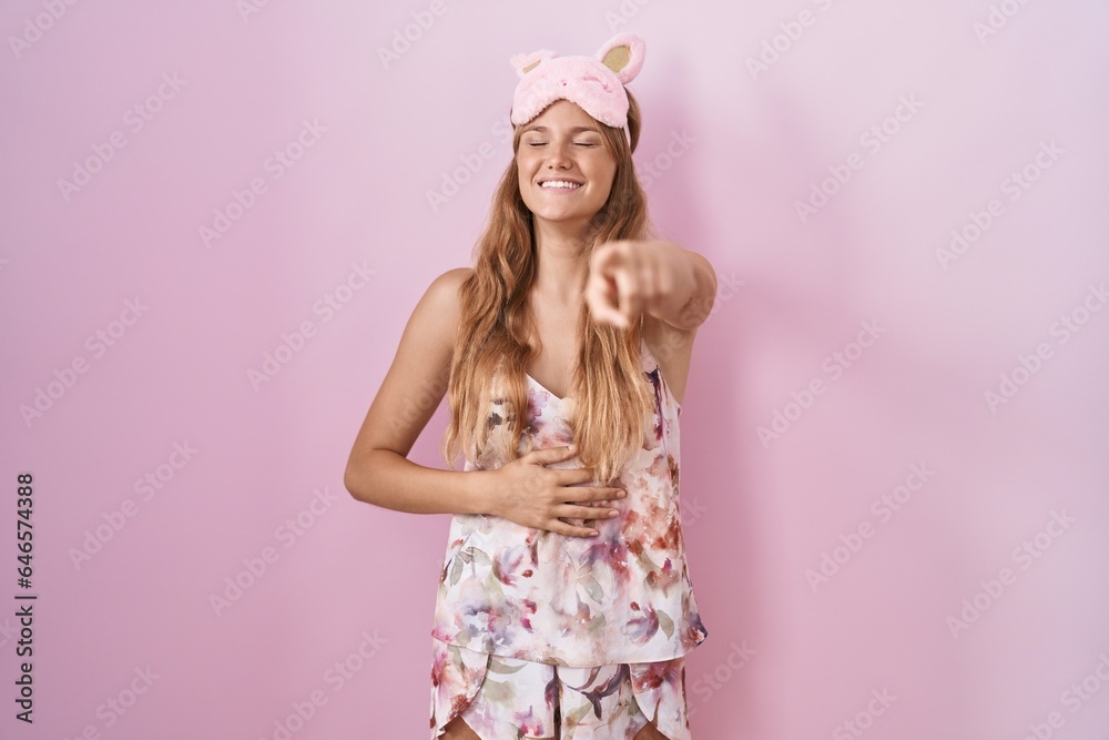 Sticker Young caucasian woman wearing sleep mask and pajama laughing at you, pointing finger to the camera with hand over body, shame expression