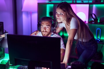 Young couple playing video games smiling looking to the side and staring away thinking.