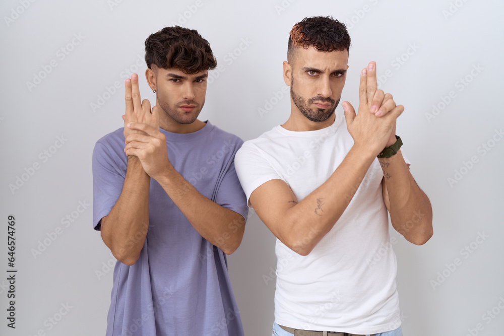 Sticker Homosexual gay couple standing over white background holding symbolic gun with hand gesture, playing killing shooting weapons, angry face