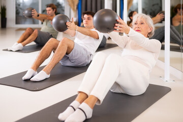 Sporty men and women doing pilates exercises with fitness ball at gym