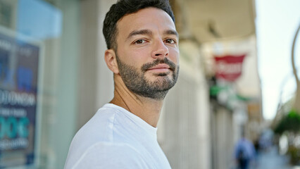 Young hispanic man standing with serious expression at street