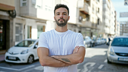 Young hispanic man standing with serious expression and arms crossed gesture at street