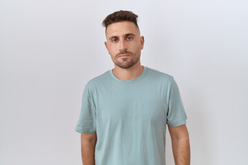 Hispanic man with beard standing over white background relaxed with serious expression on face. simple and natural looking at the camera.