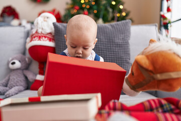 Adorable caucasian baby sitting on sofa by christmas tree with relaxed expression at home