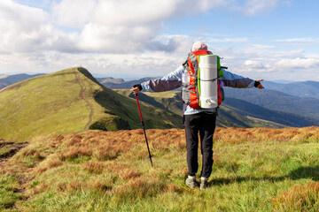 girl with backpack and hiking equipment stands and looks at the top of the mountain, woman tourist...