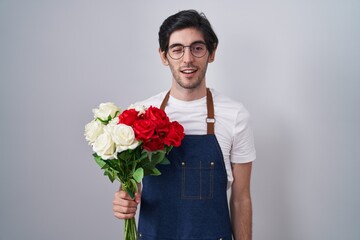 Young hispanic man holding bouquet of white and red roses winking looking at the camera with sexy...