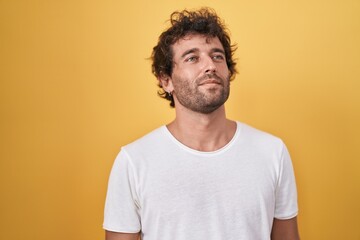 Young hispanic man standing looking to the side over isolated yellow background