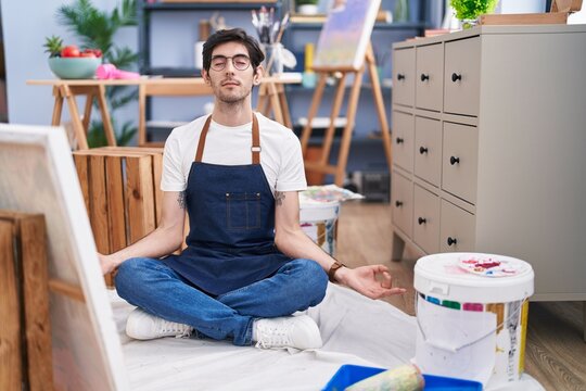 Young hispanic man artist relaxed doing yoga exercise at art studio