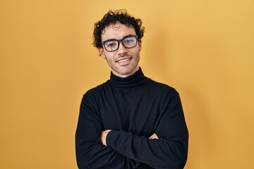 Obraz premium Hispanic man standing over yellow background happy face smiling with crossed arms looking at the camera. positive person.