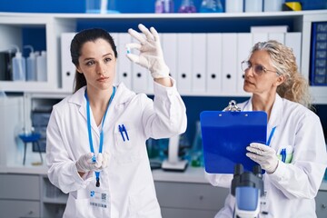 Two women scientists holding pills write on document at laboratory