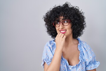 Fototapeta na wymiar Young brunette woman with curly hair wearing glasses over isolated background looking stressed and nervous with hands on mouth biting nails. anxiety problem.