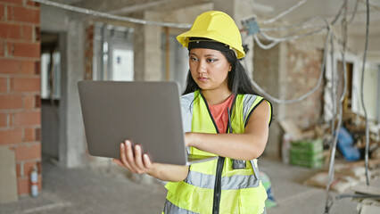 Young chinese woman architect using laptop at construction site